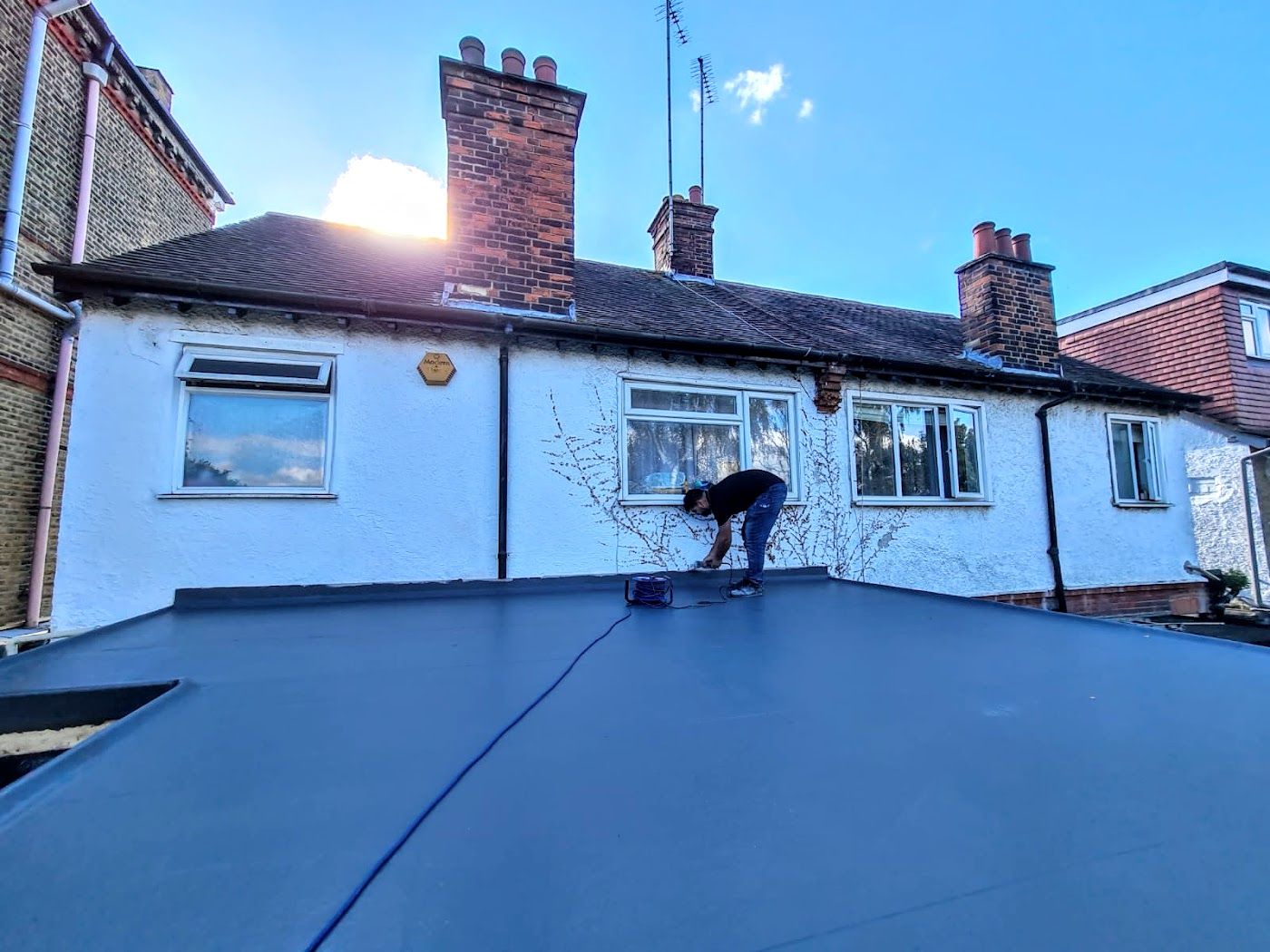 Roofer laying a blue waterproof membrane on a flat roof beside a white London house